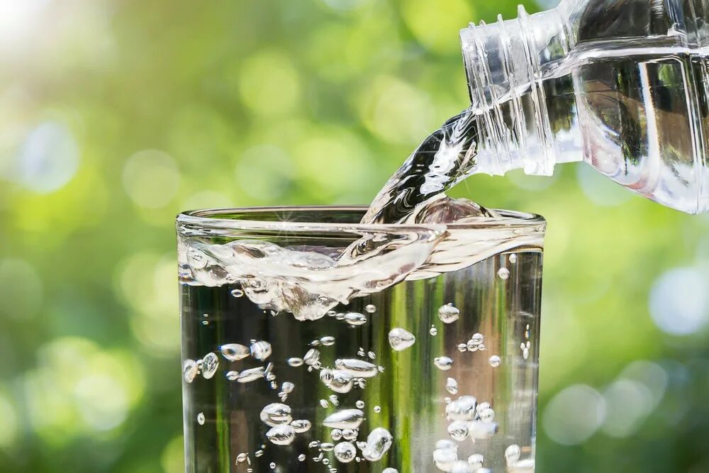 Питьевая вода. Вода льется в стакан. Стакан воды на фоне природы. Чистая вода.