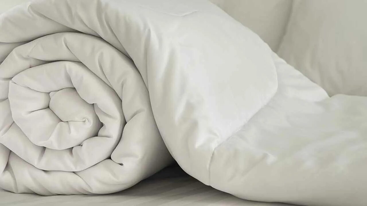Одеяло. Бежевое одеяло. Атласное пуховое одеяло. Бежевое одеяло со складками.
