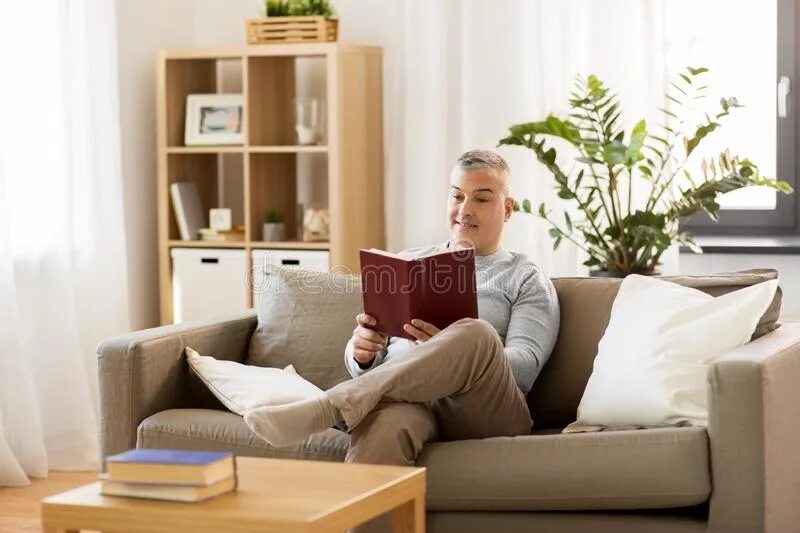 Читаем бай. Мужчина сидит в Светлом. Робот on the Couch and reading a newspaper. Чтение дома стоковые фото. Человек в интерьере сидит и читает книгу.