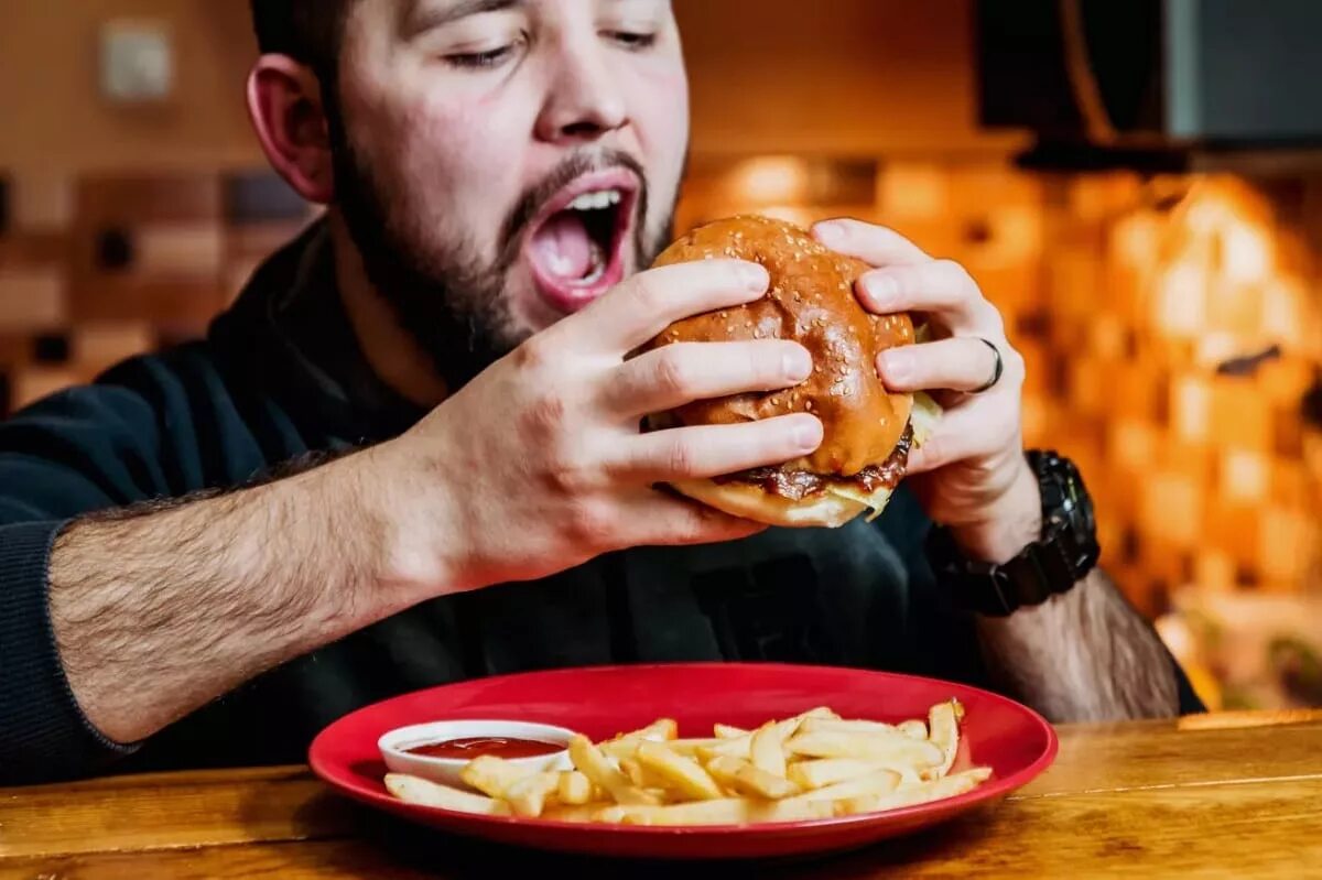 Покажи где едят. Человек ест бургер. Человек ест гамбургер. Люди едят бургеры. Мужчина ест фаст фуд.