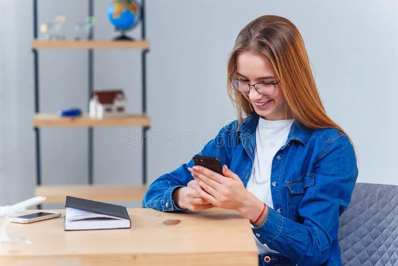 She is sitting at the table. Студентка сидит за столом. Девушка за столом голубой. Девушка в джинсовой рубашке сидит за столом. Студентка сидит на столе.