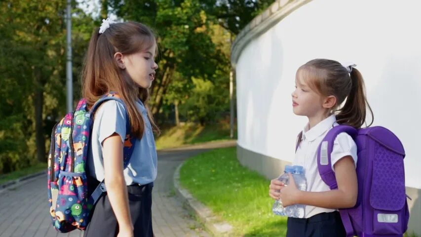 Happy schoolgirl in uniform with Backpack Feeds a Squirrel in the Park on her way to School.. Little school children