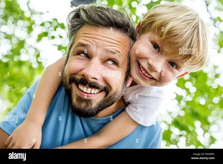 Happy father gives child piggyback ride and has fun in the park Stock Photo...