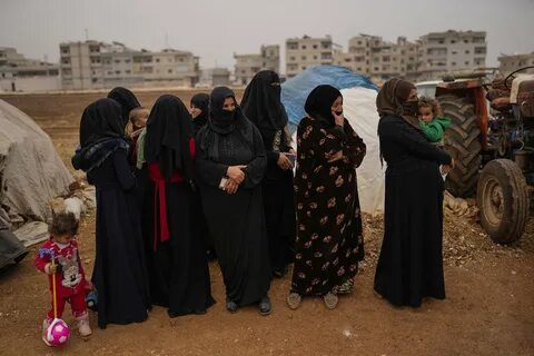 Syrian women wait for donated food to be distributed in a refugee camp for ...