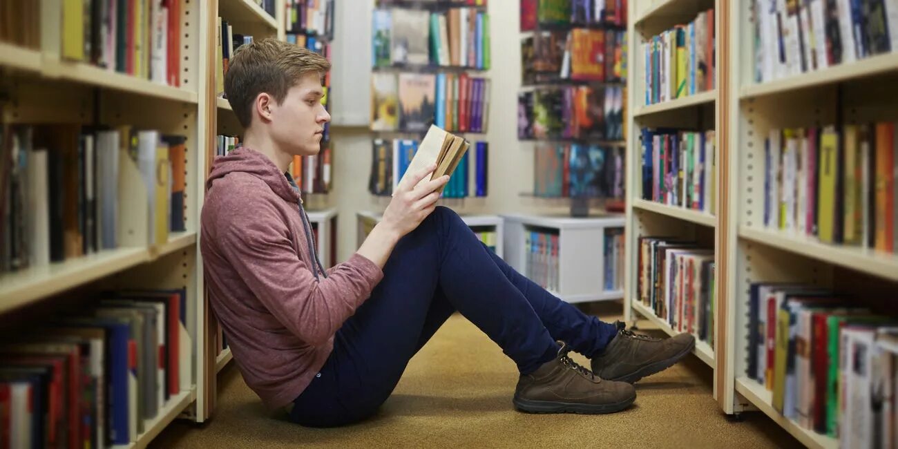 Книга ее студент. Подросток с книгой в библиотеке. Парень в библиотеке. Люди в библиотеке. Читатели в библиотеке.