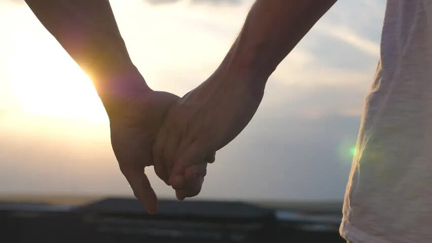 Две руки на фоне солнца. Держатся за руки на фоне моря. Двое на крыше за руки. Пара держится за руки на фоне моря.