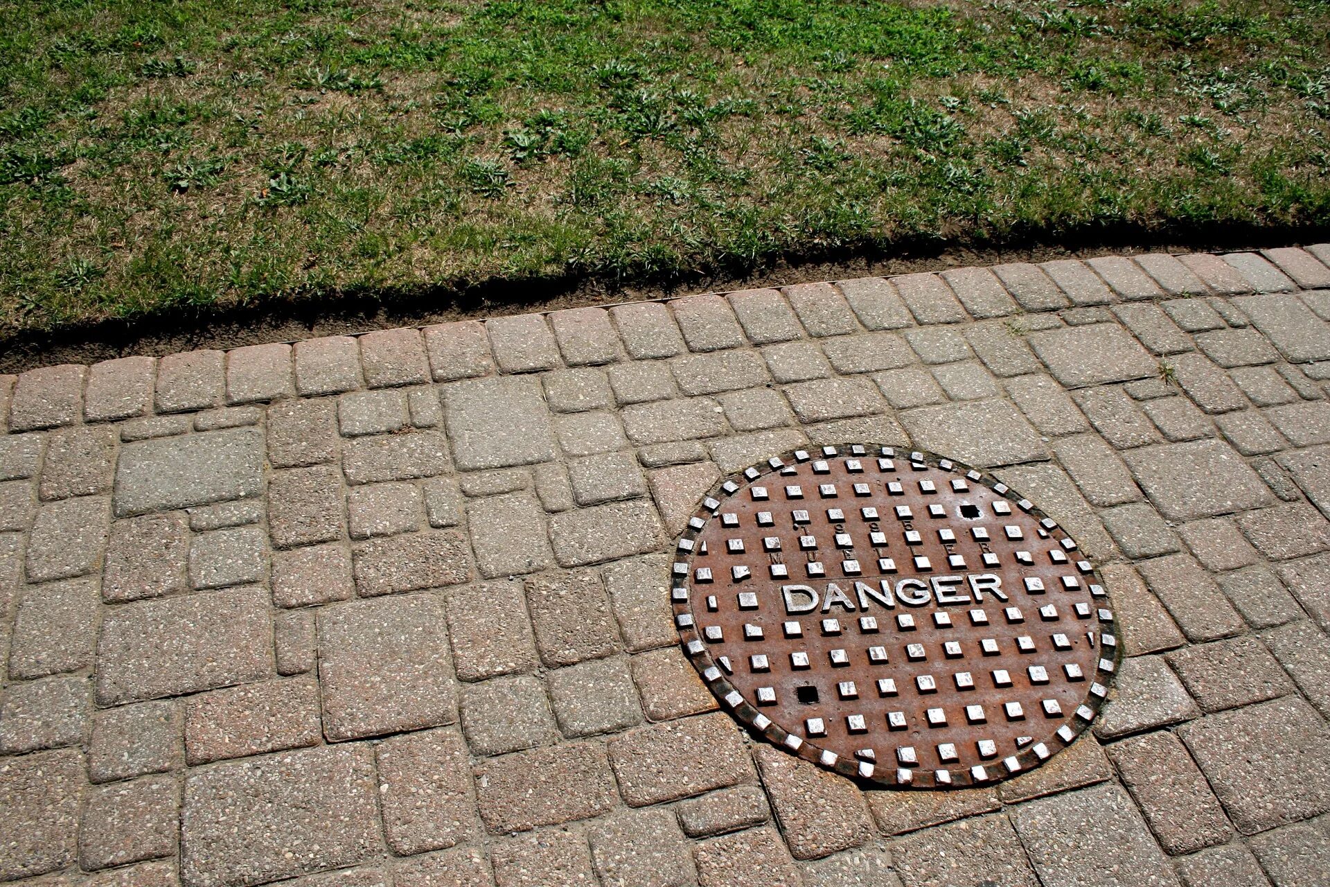 Всегда круглое. Канализационный люк на тротуаре. Брусчатка вокруг канализационного люка. Тротуарная плитка возле канализационного люка. Люк канализации на тротуаре.