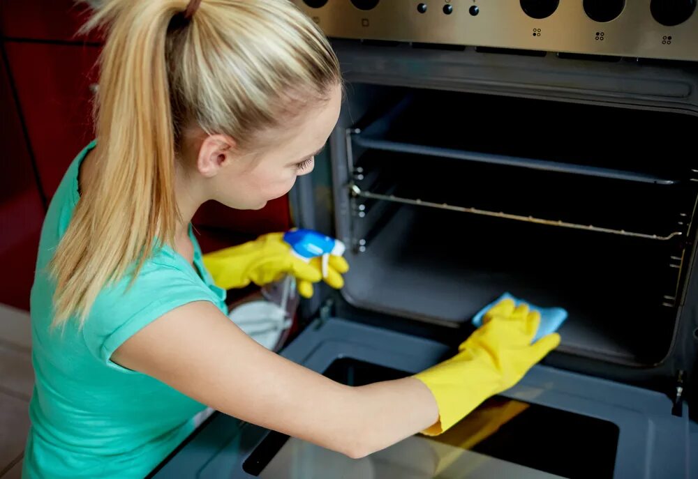 Oven Cleaning. Мытье духовки. Девушка моет духовку. Хозяйка чистит духовку.