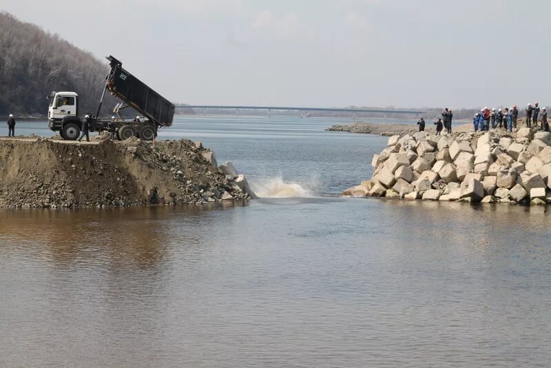 Люди перегородили реку большой плотиной вода выше. Бурея ГЭС. Водная блокада Крыма. Отсыпка дамбы. Насыпная дамба.