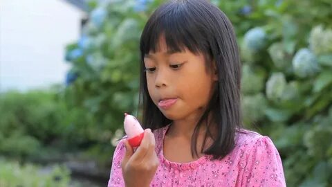 A cute little 6 year old Asian girl enjoys licking her popsicle on a hot su...