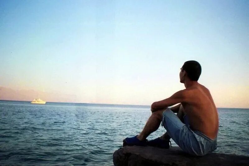 Мужчина сидит на берегу. Парень сидит на берегу моря. Человек сидит на берегу. Человек сидит на берегу моря.