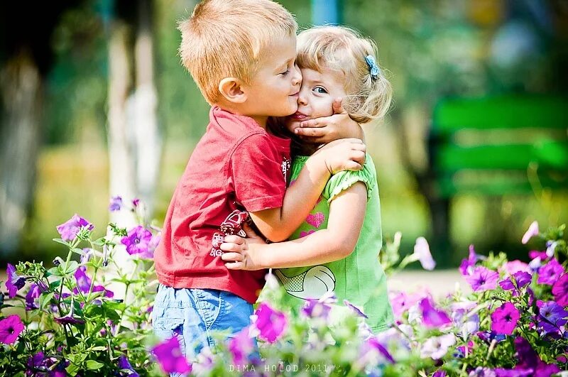 Детский поцелуй. Мальчик и девочка любовь. Мальчик обнимает девочку. Мальчик с девочкой в траве. Влюбленные детки.