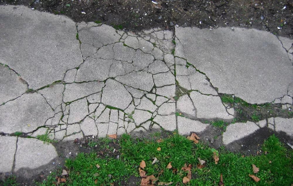 Бетонная дорожка растрескалась. Потрескались бетонные дорожки. Бетон с камнями. Сломанный камень.