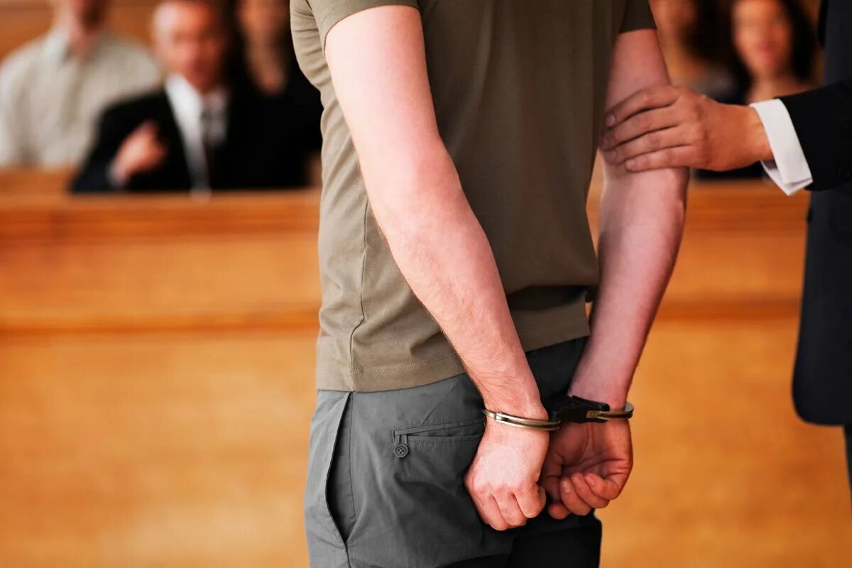 Касается обвиняемого. Мужчина в наручниках в зале суда. Подросток в суде.