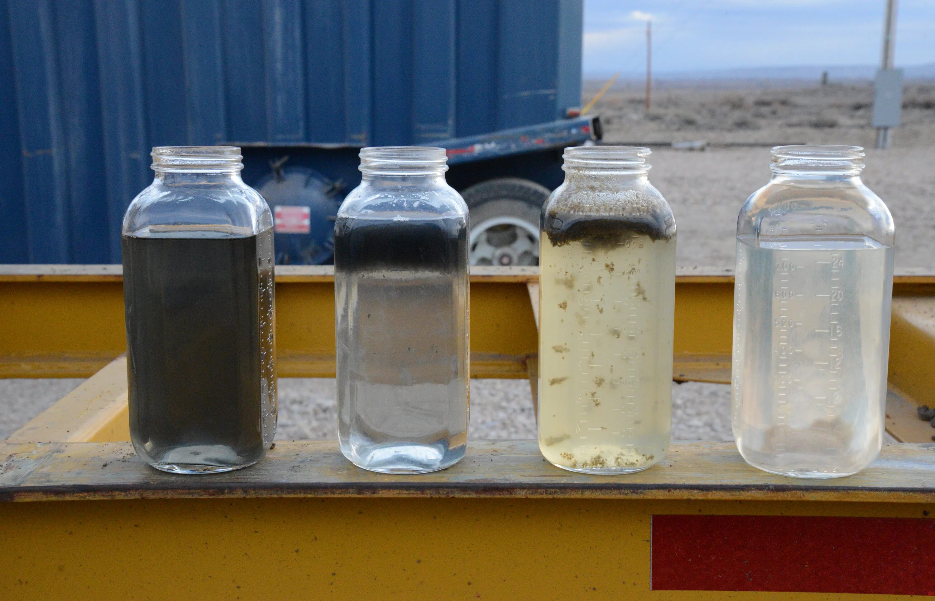 Стеклянные бутылки для отбора проб нефтепродуктов. Расслоение жидкости. Пробы загрязненной воды. Осадок нефтепродуктов.