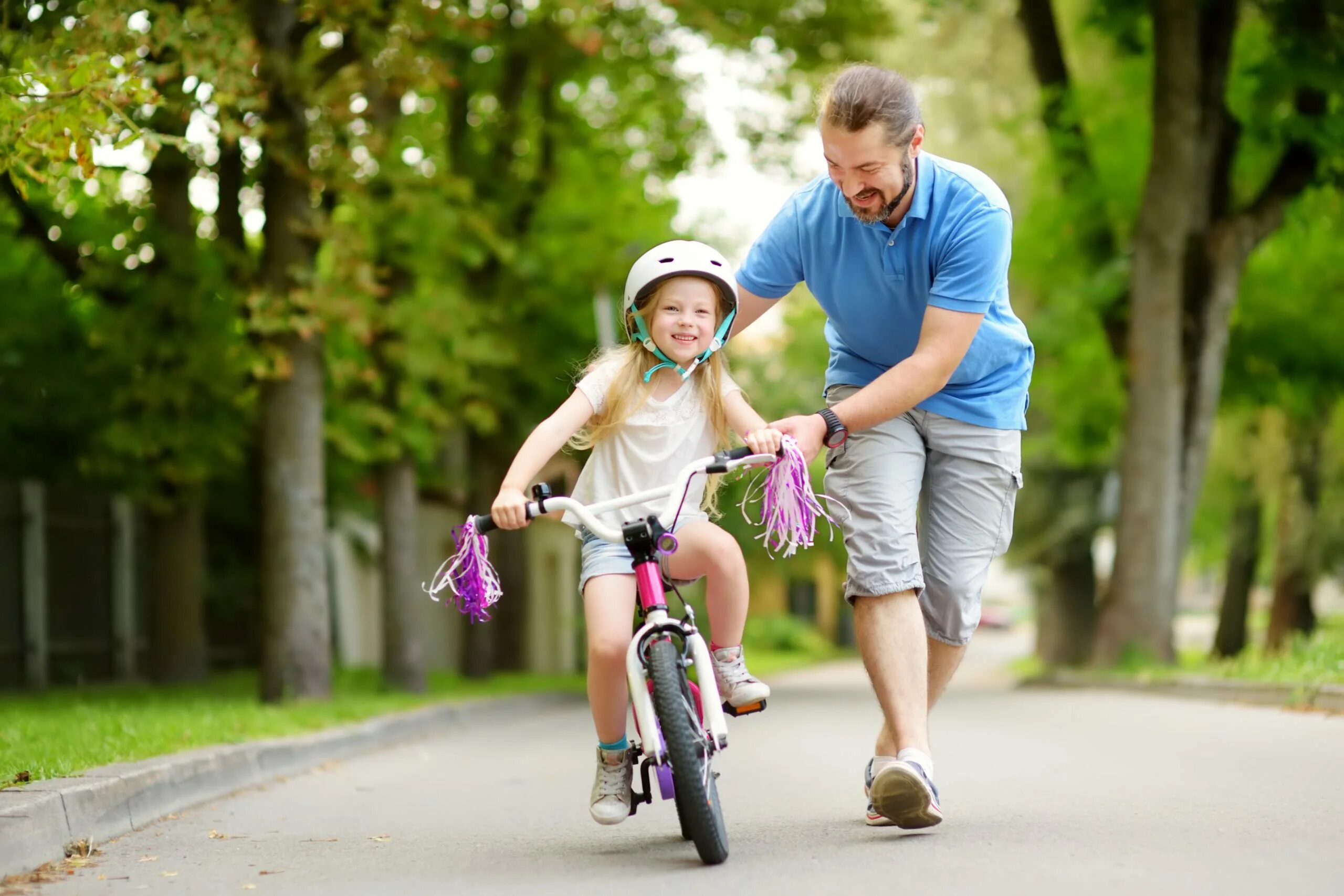 The children are riding bikes. Велосипеды для всей семьи. Папа с ребенком на велосипеде. Отец учит ребенка кататься на велосипеде. Папа и дочь на велосипеде.