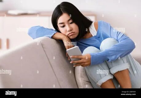 Frustrated asian lady checking mobile phone sitting on the couch Stock Phot...