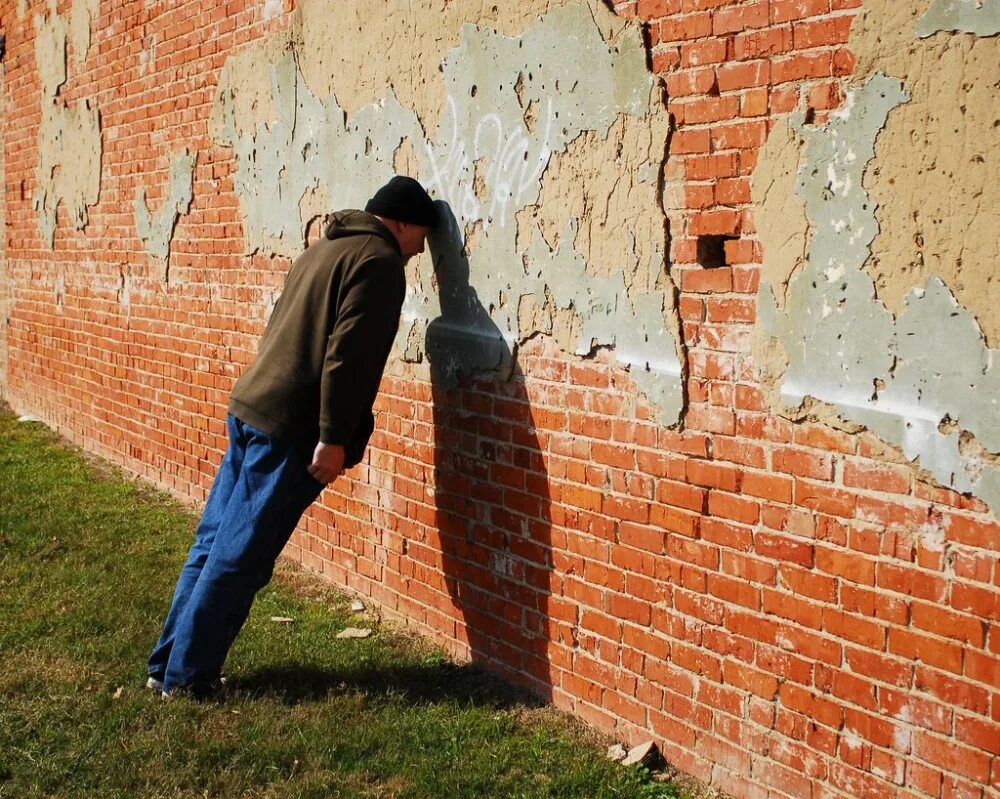 Стоит огромная стена. Головой об стену. Человек перед кирпичной стеной. Человек у стены. Человек уперся в стену.