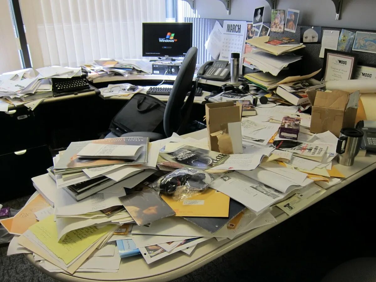 Много бумаг на столе. Стол заваленный бумагами. Письменный стол заваленный бумагами в офисе. Бардак на рабочем месте. Беспорядок на офисном столе.