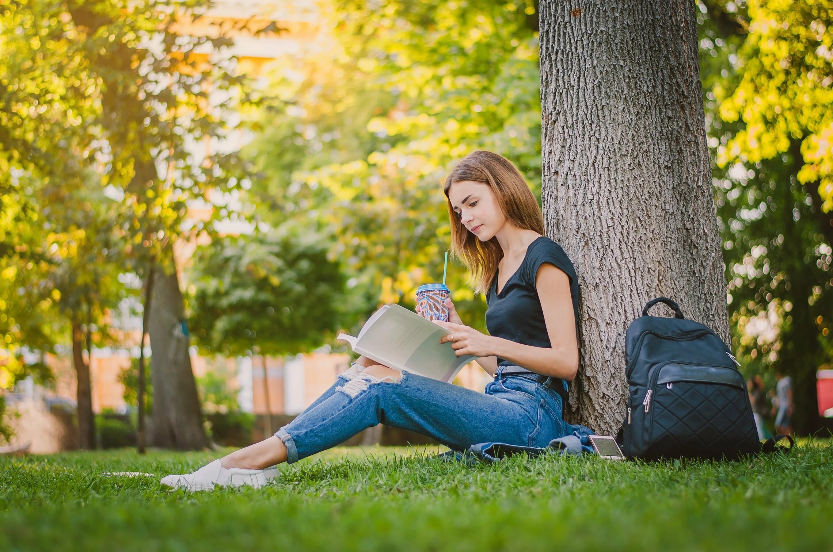 Students sitting on the grass. KMAT student sitting. A girl sitting outdoors with a Laptop. Man reading a book on the grass.