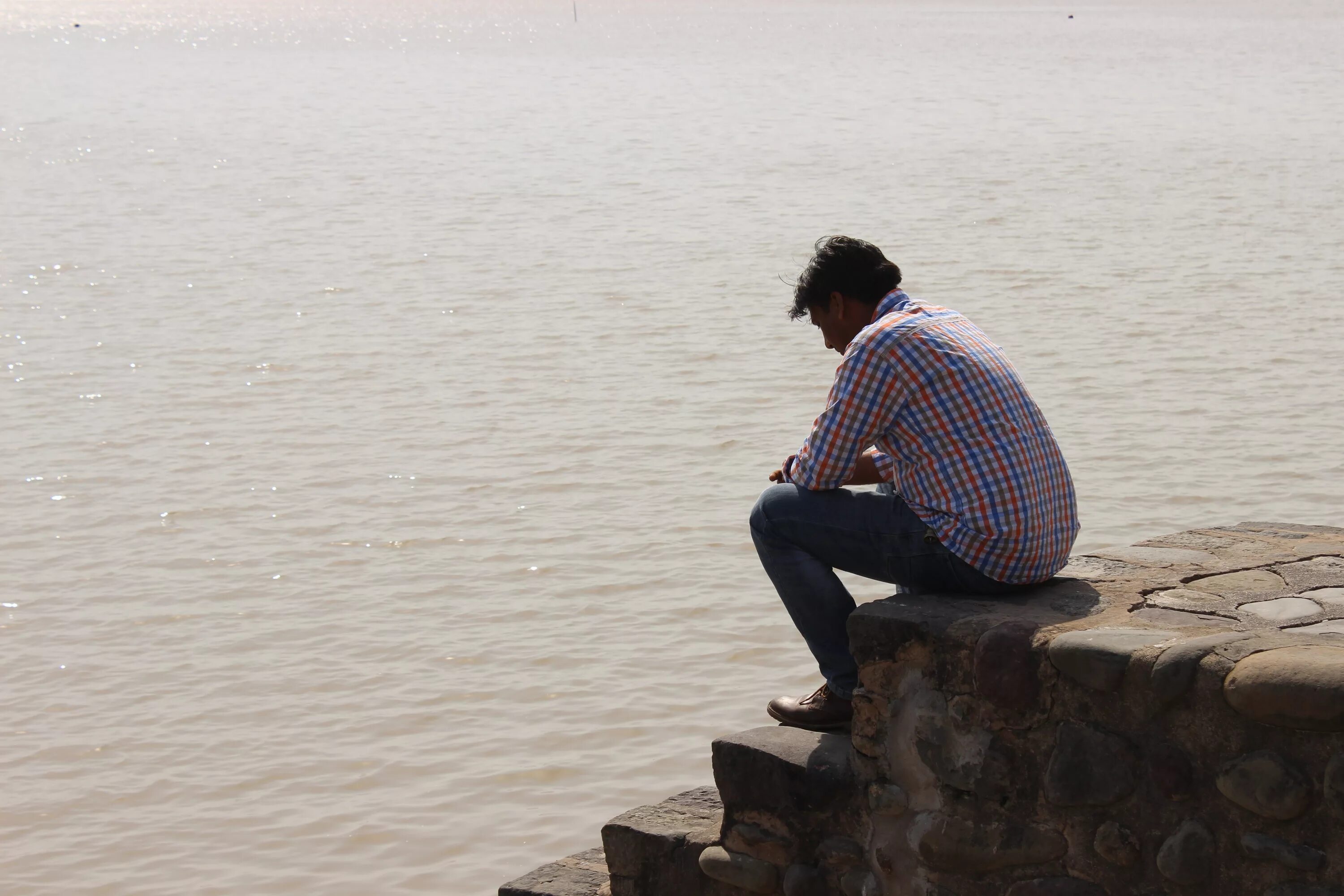 Человек возле реки. Человек сидит на Камне. Человек сидит на берегу. Парень сидит на Камне. Сидит на берегу моря.