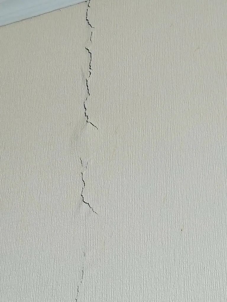 Как заделать трещины в квартире. Трещина в стене в квартире. В новостройке трещина в стене в квартире. Вертикальная трещина на белой стене. Аварийные трещины в квартире.