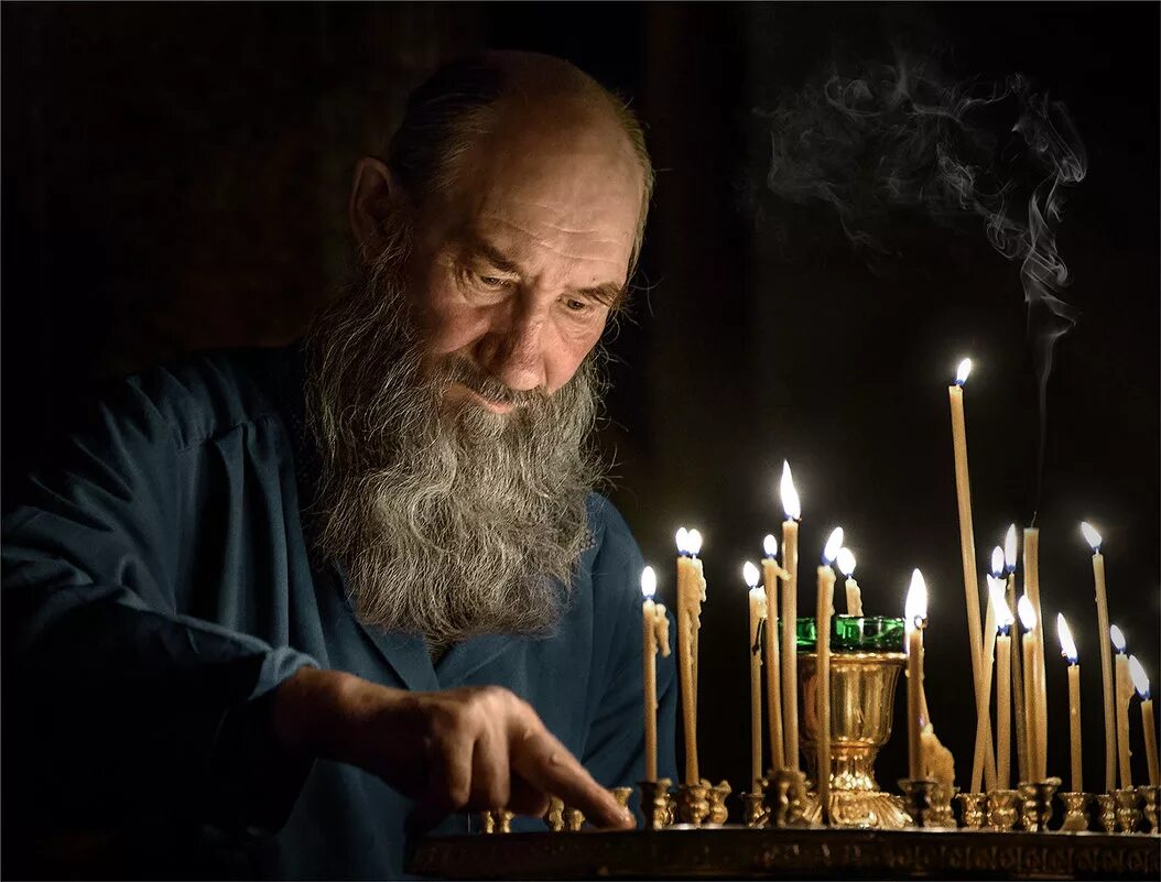 Мужчина ставит свечу. Старик молится в церкви. Православный человек молится. Старик в храме. Дедушка молится в храме.