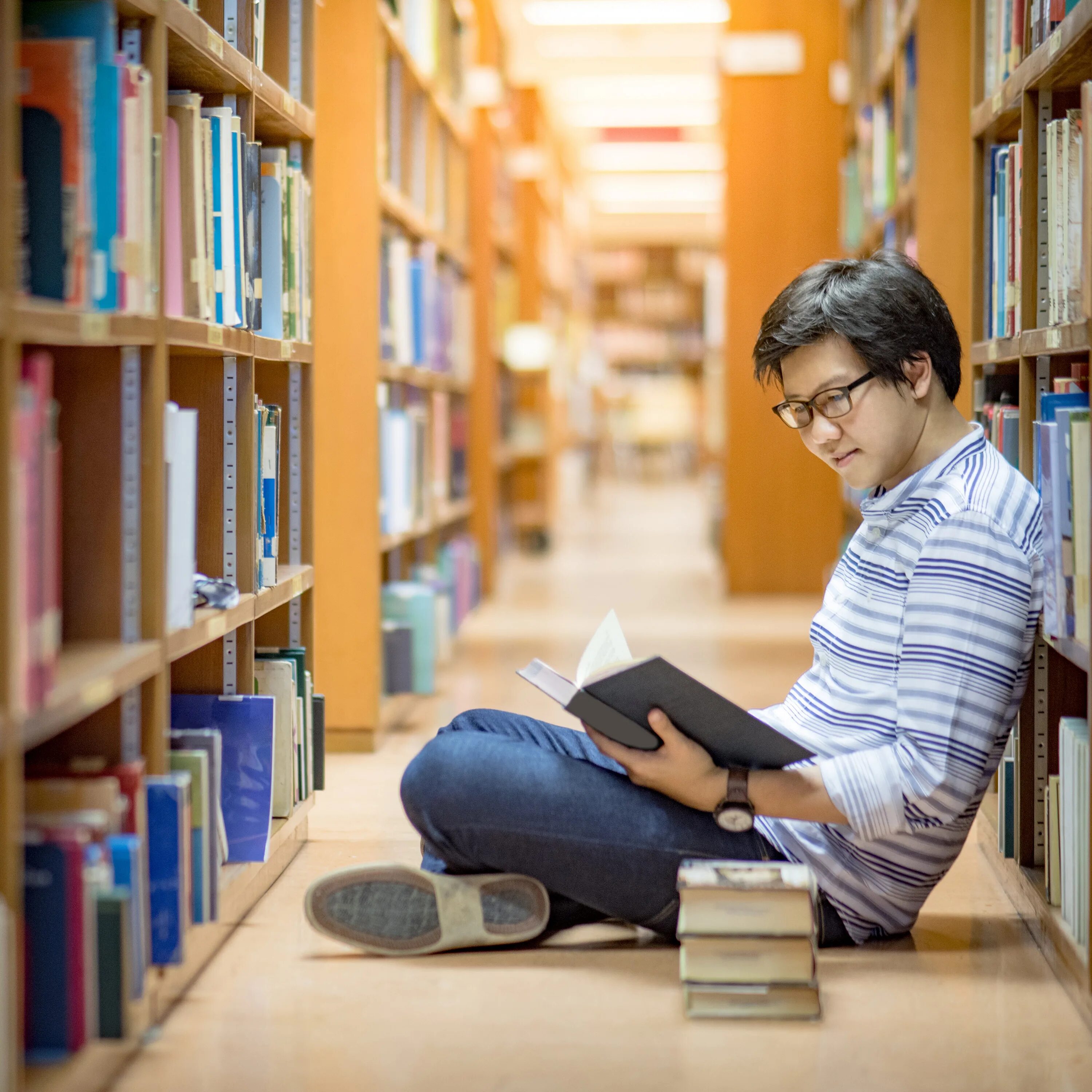 Студент работает в библиотеке со специальной. Нетворкинг в библиотеке. students at the library. парень азиат с книгами. азиатские книги лучшие.