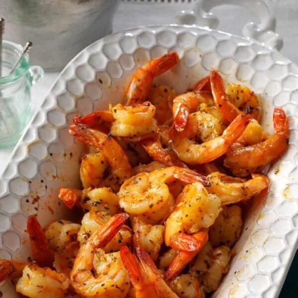 Glass baking dish filled with bake shrimp and garlic butter sauce, garnished wit