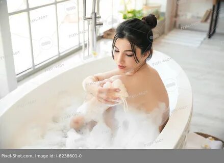 Pretty young woman taking bath with loofah at home. 