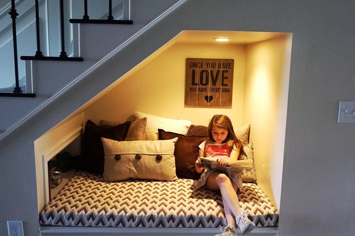 Как меньше бывать дома. Спальное место под лестницей. Домик под лестницей для ребенка. Уютный уголок под лестницей. Уголок для чтения под лестницей.