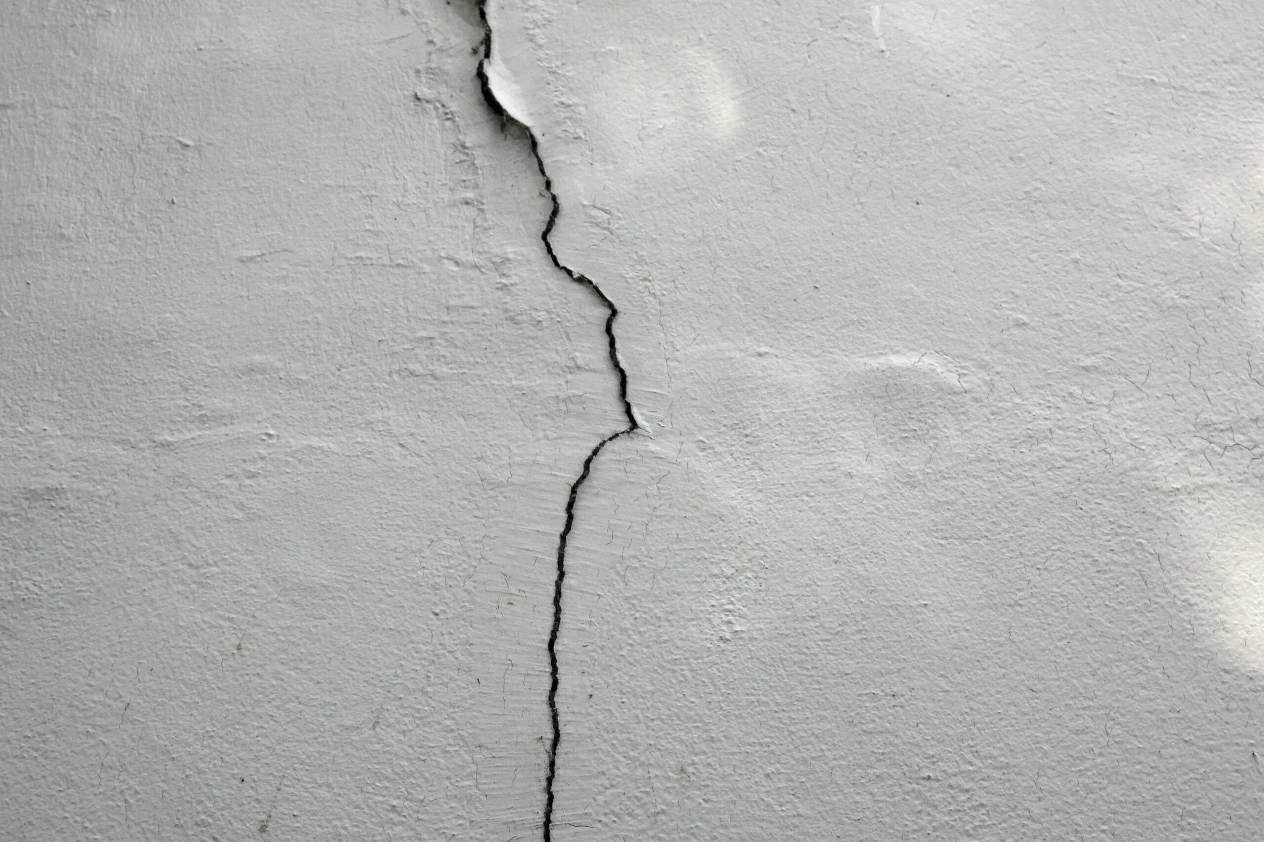 Причина появления трещины. Трещины в бетоне. Трещина в стене. Бетонная стена с трещинами. Белая стена с трещинами.