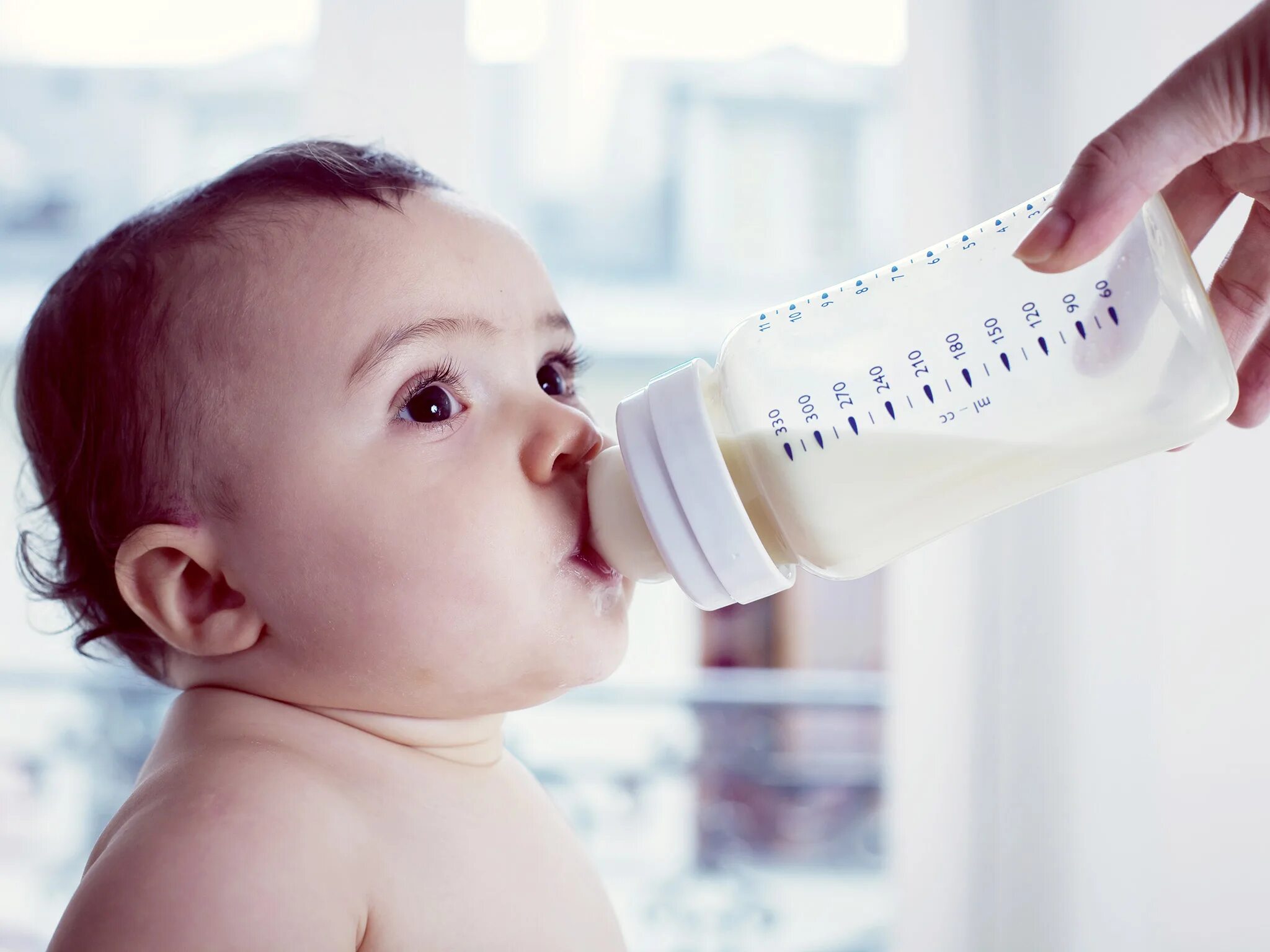 Искусственное вскармливание детей. Малыш пьет из бутылочки. Малыш с бутылочкой. Малыш с бутылкой молока.
