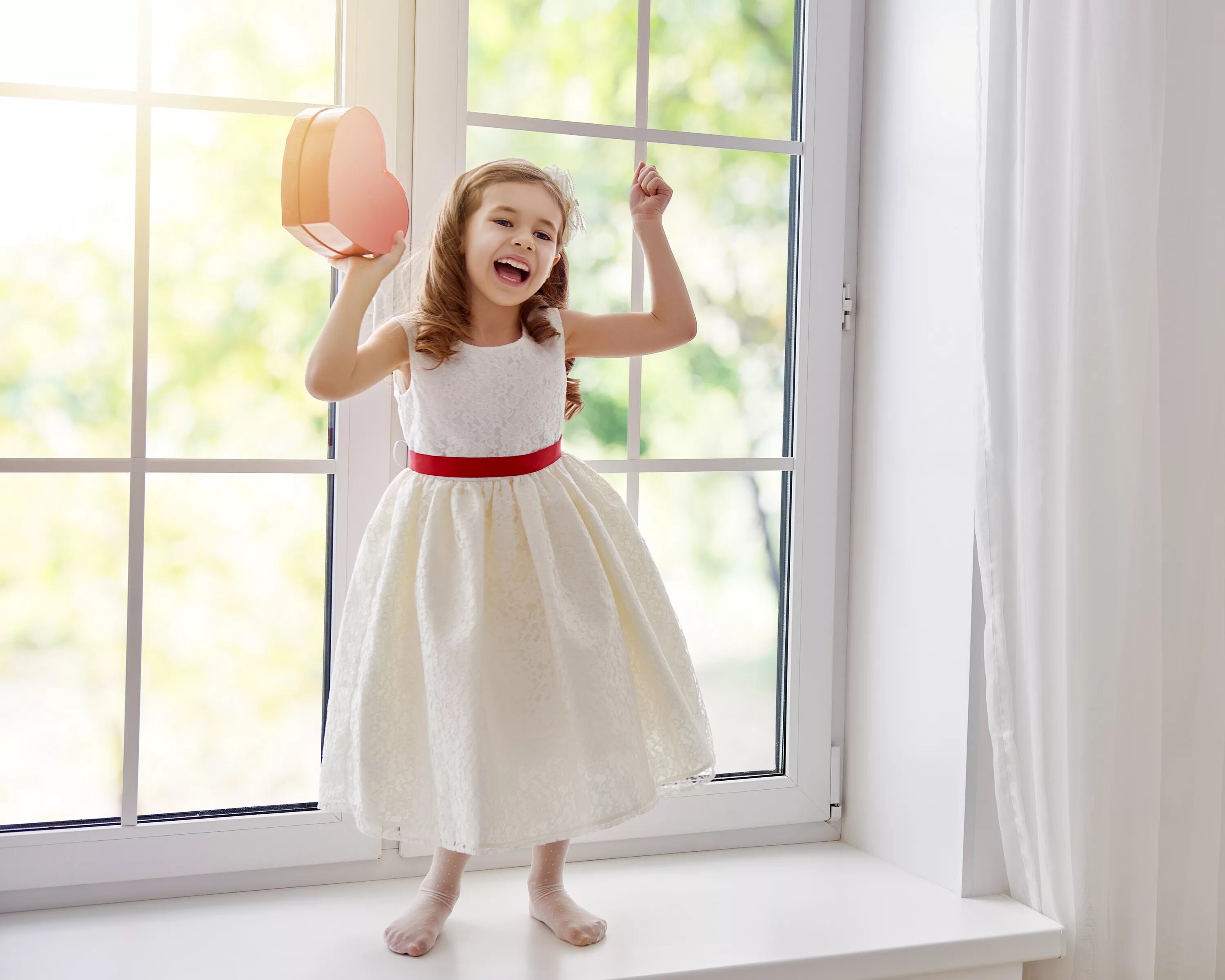 Счастливый ребенок у окна. Маленькая девочка на подоконнике. Девочка в платье у окна. Девочка на окне с сердечком.