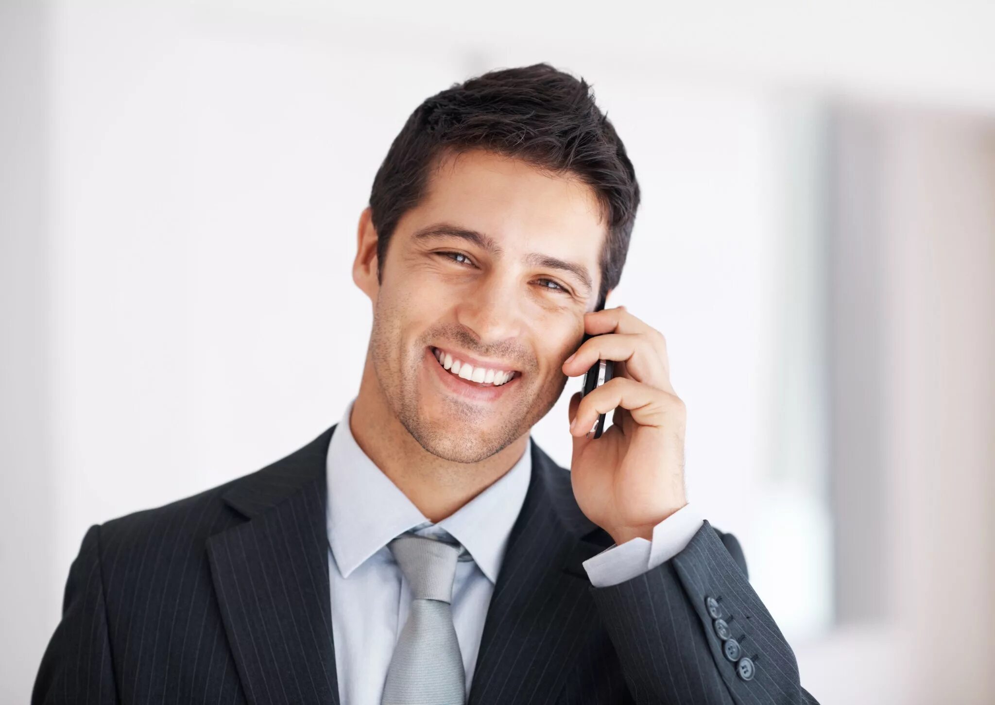 Человек смотрит и улыбается. Бизнесмен с телефоном. Мужчина улыбается. Деловой мужчина. Бизнесмен улыбается.