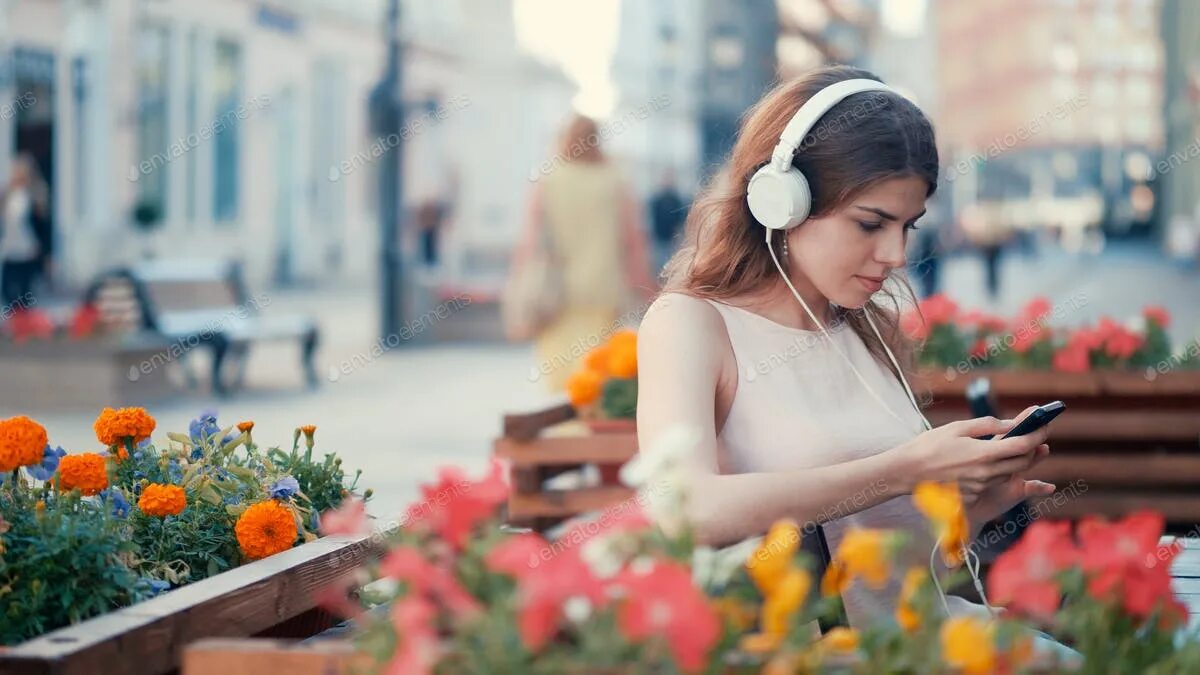 Парк чтения. Счастливая девушка в наушниках. Девушка прислушивается. Downloading a song. Listen the girls are.