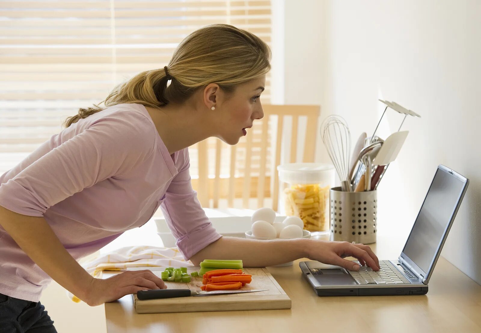 Женщина на кухне за ноутбуком. Девушка за ноутбуком на кухне. Домохозяйка за компьютером. Женщина работает дома.
