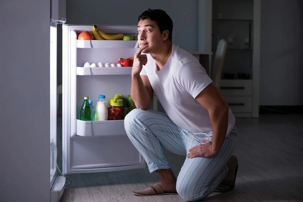 Мужчина заглядывает в холодильник. Холодильник с едой. Человек ест ночью.