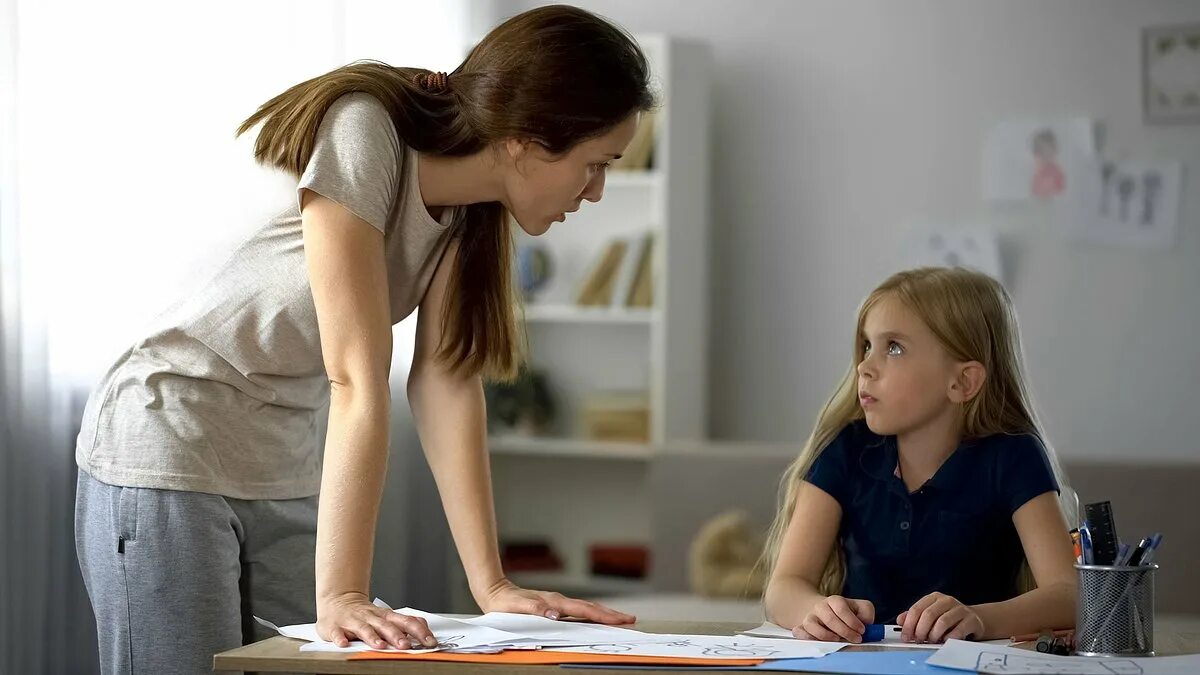 Disciplining daughters. 2 девочки учат уроки и рядом мама. Ребенок подсматривает за родителями. Мама была строга. Мама ругается.