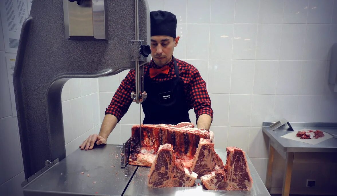 Portrait of a handsome butcher in white uniform at the meat manufacturing with p