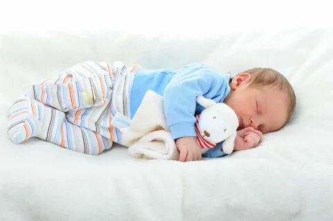 a baby laying on top of a bed next to a stuffed animal.