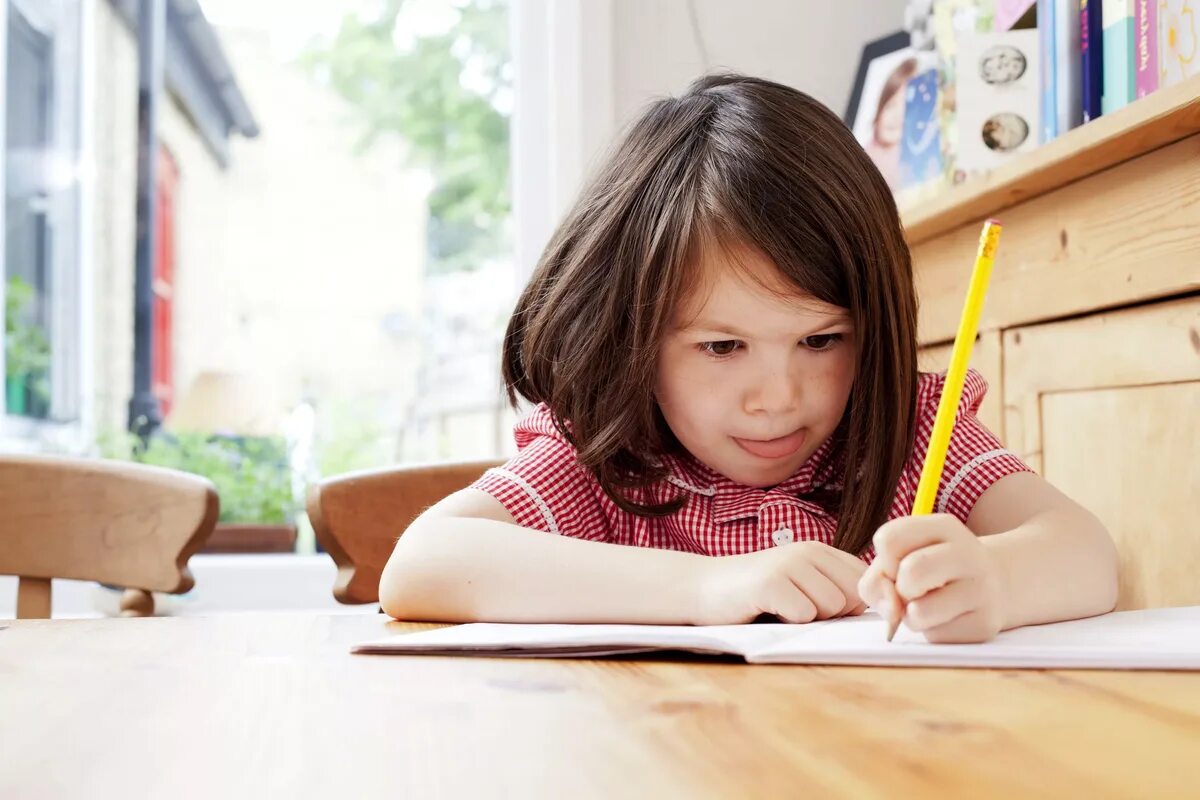 Маленький ребенок делает уроки. Ребенок пишет. Старательный ребенок. Дети сочиняют. Девочка учит уроки.