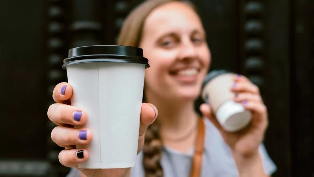 стакан для кофе. стаканчик кофе в руке девушки. человек со стаканчиком кофе. девушка пьет кофе. термокружка в руке.