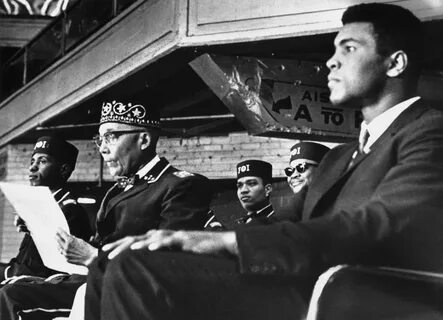 (R) sits on the podium with Nation of Islam leader Elijah Muhammad while at...