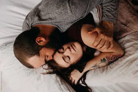 Close up of young, beautiful couple snuggled in the linen sheets of their b...