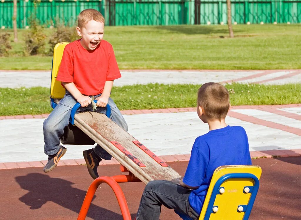 Два мальчика качаются. Дети качаются на seesaw. два мальчика на детской площадке. дети катаются на качалке. два ребенка качаются на доске.