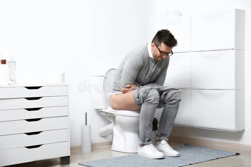 Мужчина сидит на унитазе в ванной. У парня болит живот на унитазе.