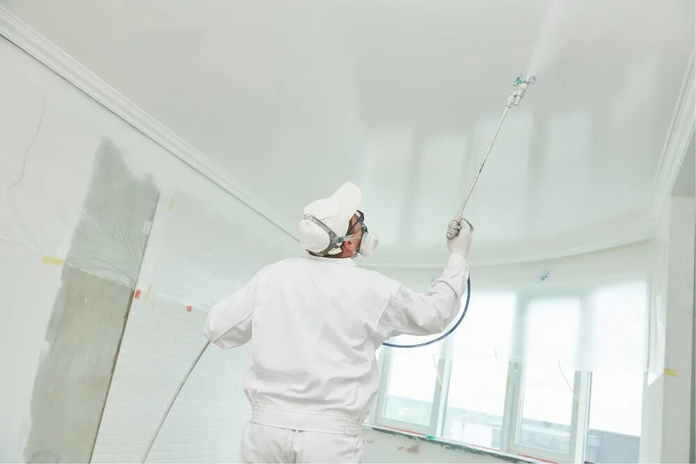 A woman on a ladder uses a paint roller to paint a ceiling.