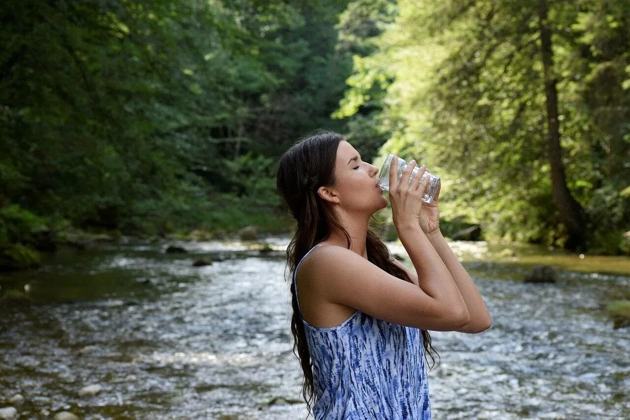 Жажда. Девушка пьет воду. Стакан воды на природе. Питьевая вода. Девушка с питьевой водой.