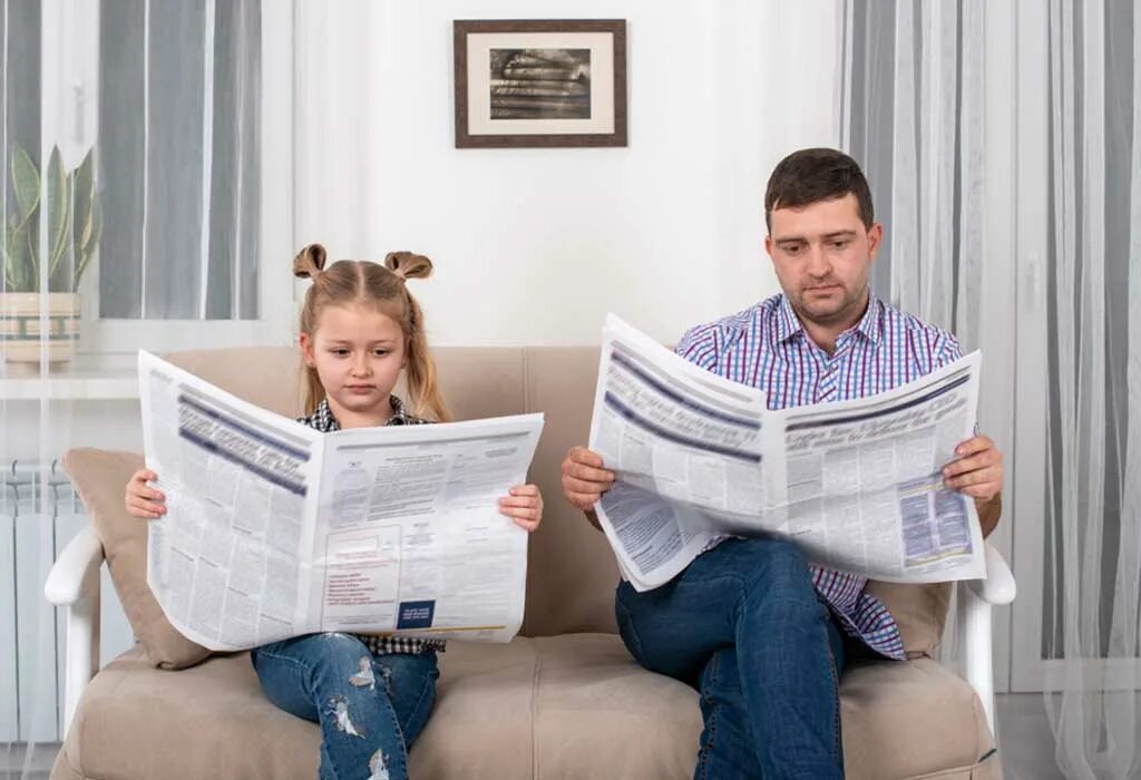 Форум читающих семей. Семья читает газету. Читает газету на диване. Папа и дочь сидит на диване. Папа читает газету.